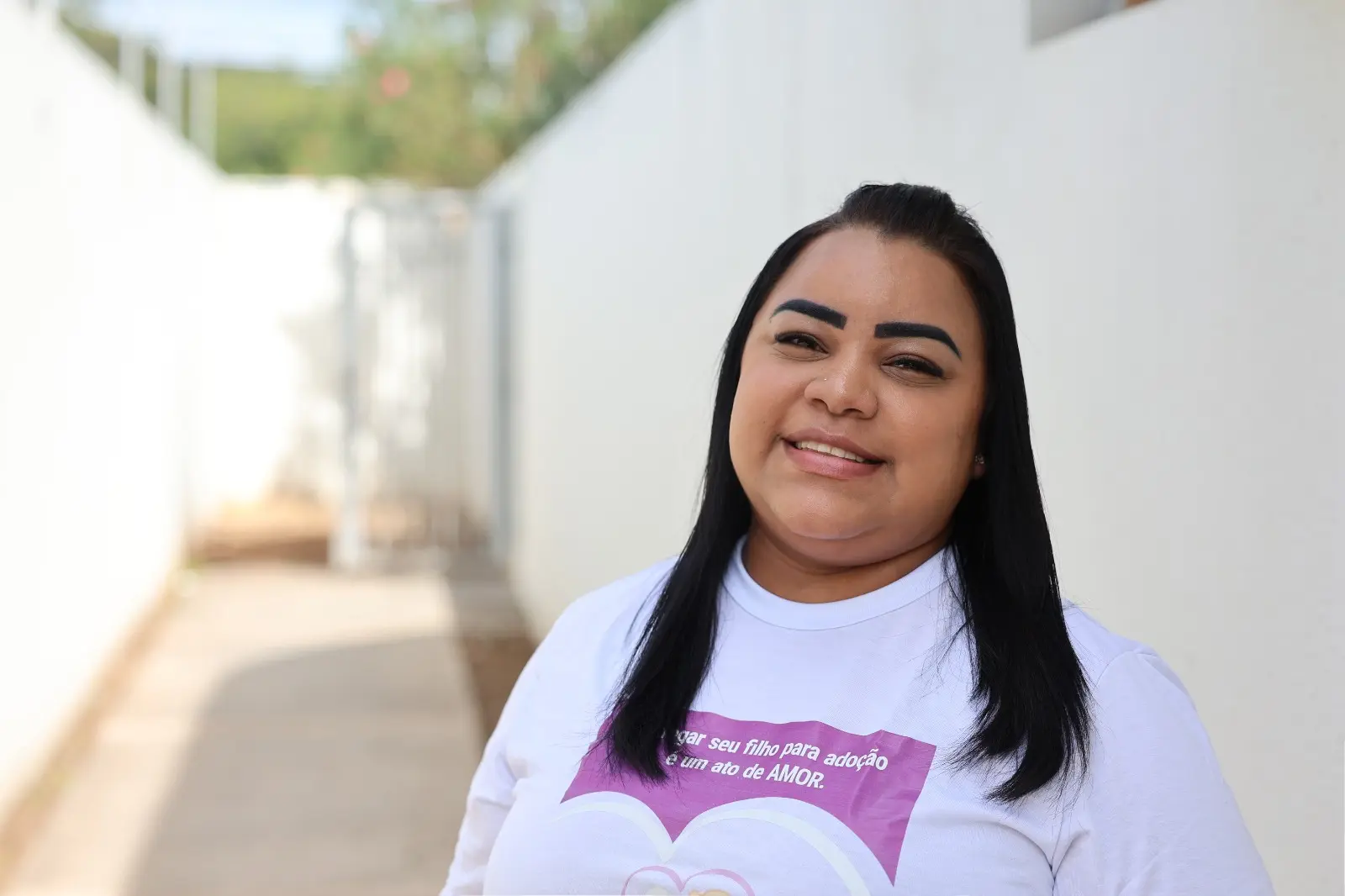 A imagem mostra a psicóloga da Vara da Infância e Juventude de Cuiabá, Marciene Aparecida dos Santos Lopes, ela sorri para a câmera e veste camiseta branca da campanha Entrega Legal, com a frase 