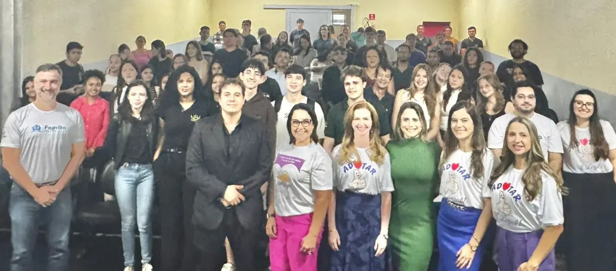 A imagem mostra um grande grupo de pessoas reunido em um auditório inclinado, posando para uma foto coletiva após o evento.