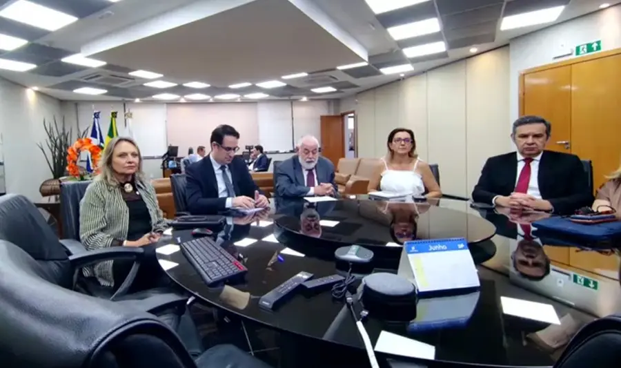 Print de tela que mostra o presidente do TJMT, juízes auxiliares e a vice-diretora geral sentados em torno de uma mesa redonda de vidro, durante reunião de lançamento da Copa do Judiciário no segundo grau.